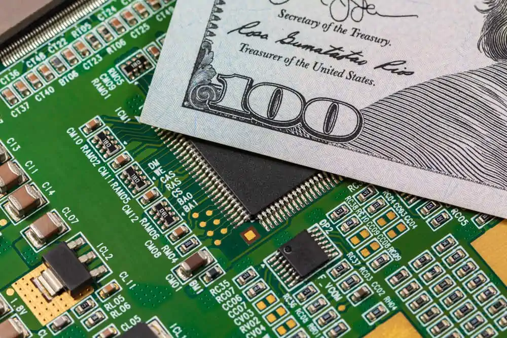 Closeup,Of,Semiconductor,Circuit,Board,And,100,Dollar,Bill.,Concept Electronic materials shortage in PCB assembly illustrated by money on a circuit board